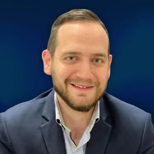 Professional portrait of Hazim, Director of Search & Email Marketing at AIWIZ, wearing a navy blazer and striped shirt against a blue background, specialising in SEO and email campaign strategy.