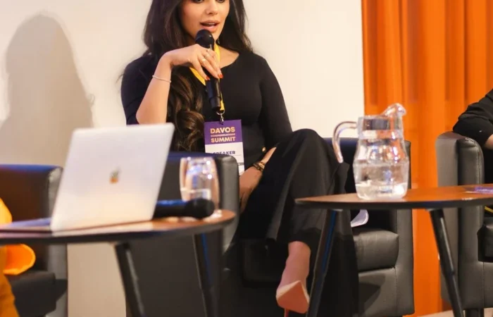 Lima Alhawamdeh speaking on digital communications panel at Davos World Summit 2025, wearing black outfit with orange-curtained backdrop
