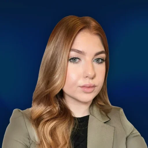 Person with red hair and blazer against blue background.