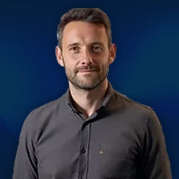 Professional portrait of Simon, Director of Paid Media & Performance Marketing at AIWIZ, wearing a charcoal button-up shirt against a blue background, specialising in Google Ads and PPC strategy.