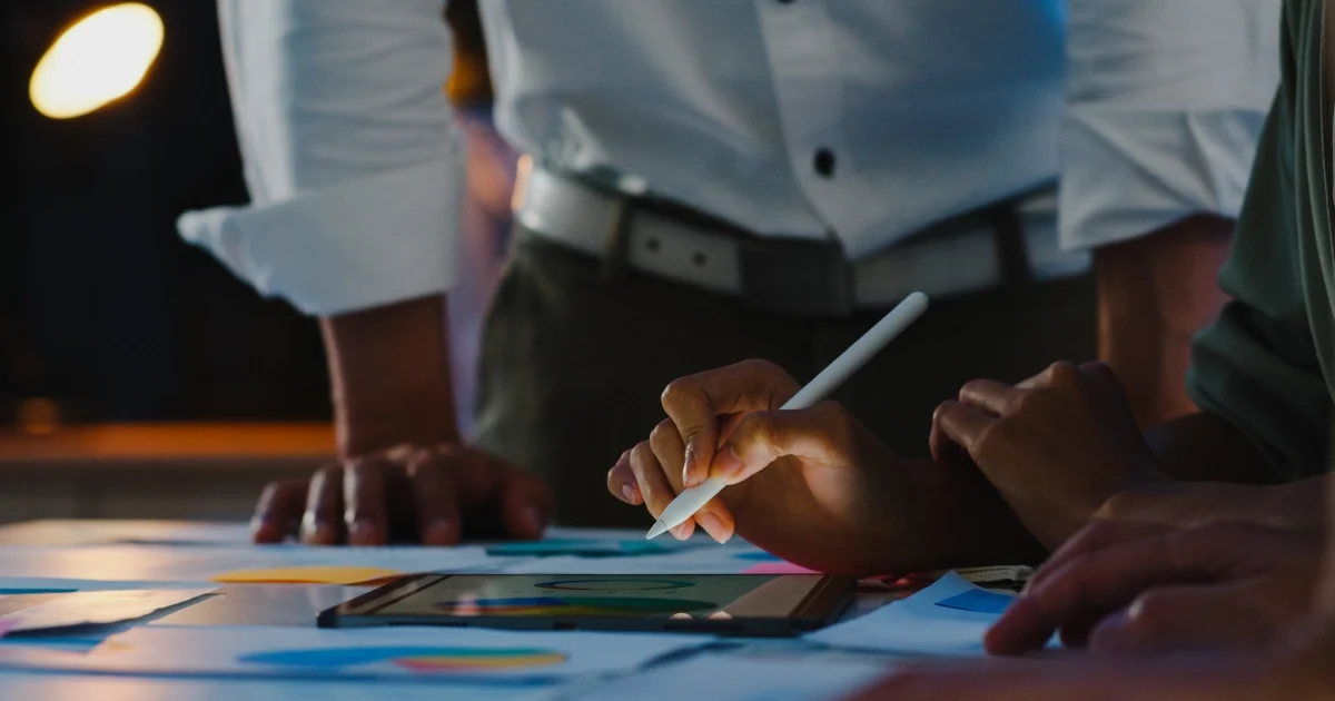 A team working together on a digital marketing plan using a tablet and other materials spread across the table.