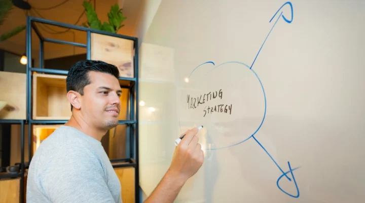 A founder writing 'Marketing Strategy' on a whiteboard with arrows branching out to channel decisions